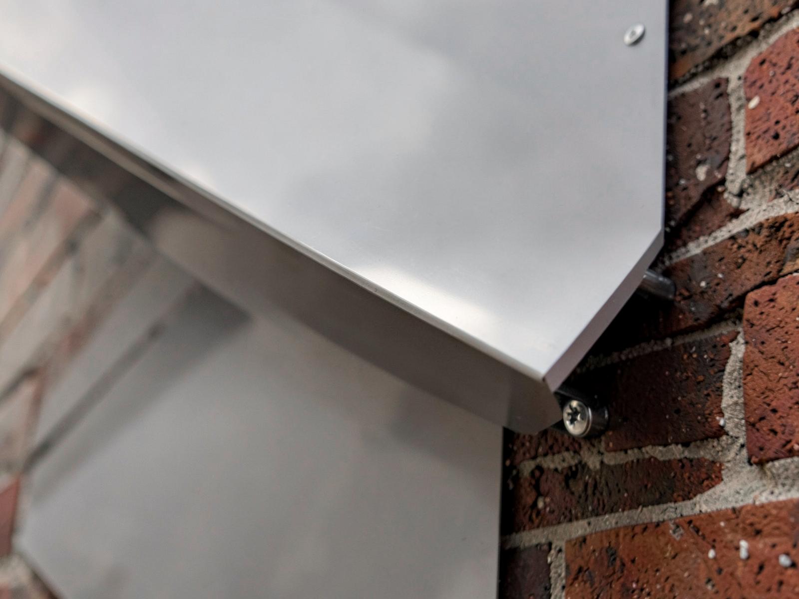 Detalj av en aluminiumpanel med distansfäste mot en tegelfasad